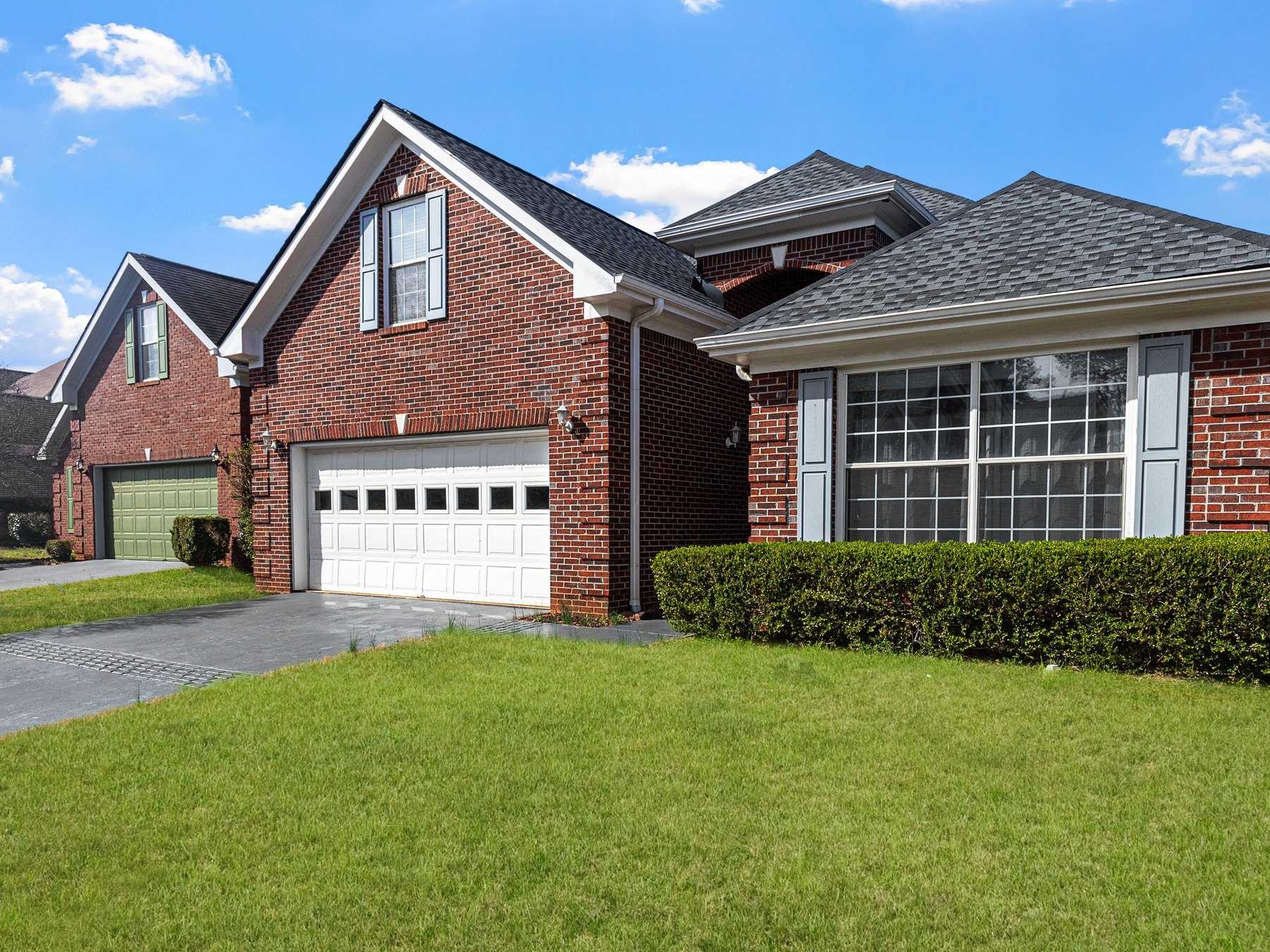 Red-brick suburban home with a white raised-panel garage door and a landscaped front lawn