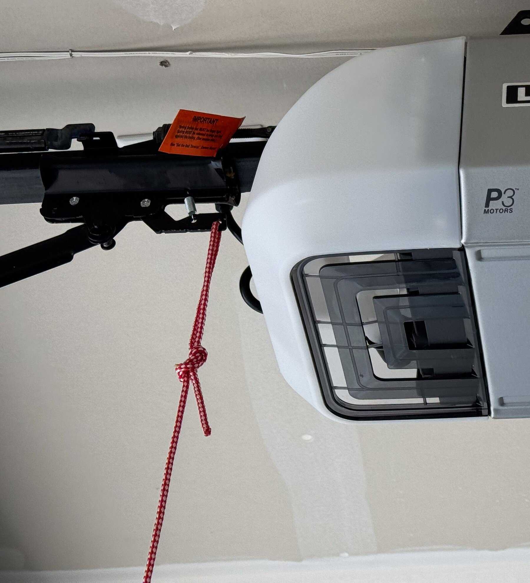 Red emergency-release cord hanging from the opener trolley beside the opener motor unit