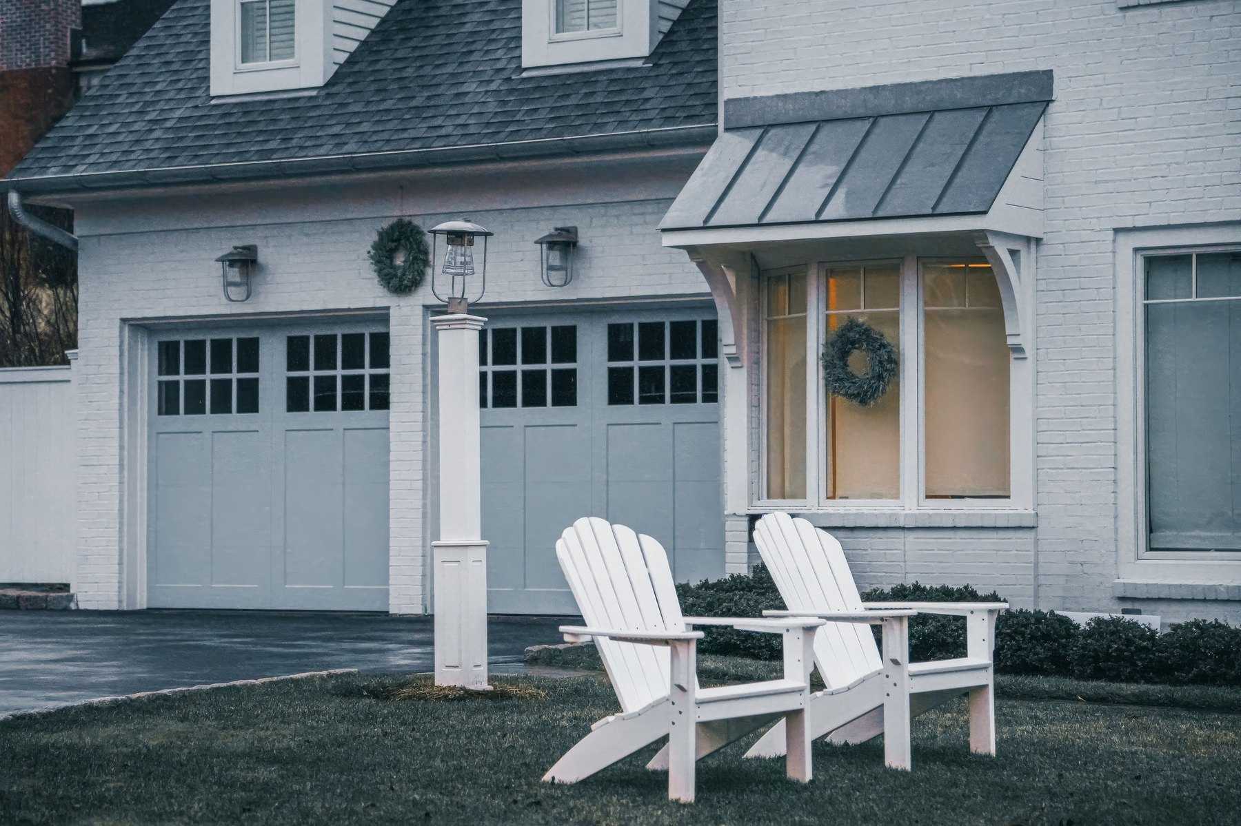 Two light-gray carriage-style garage doors with square window panels on a white-painted brick home