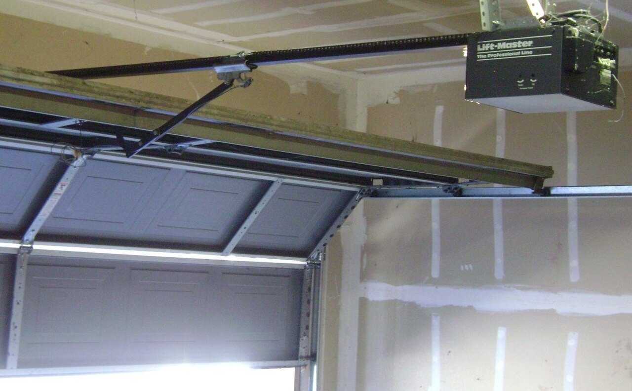 Ceiling-mounted garage door opener with its rail and door arm connected to a partly open sectional door