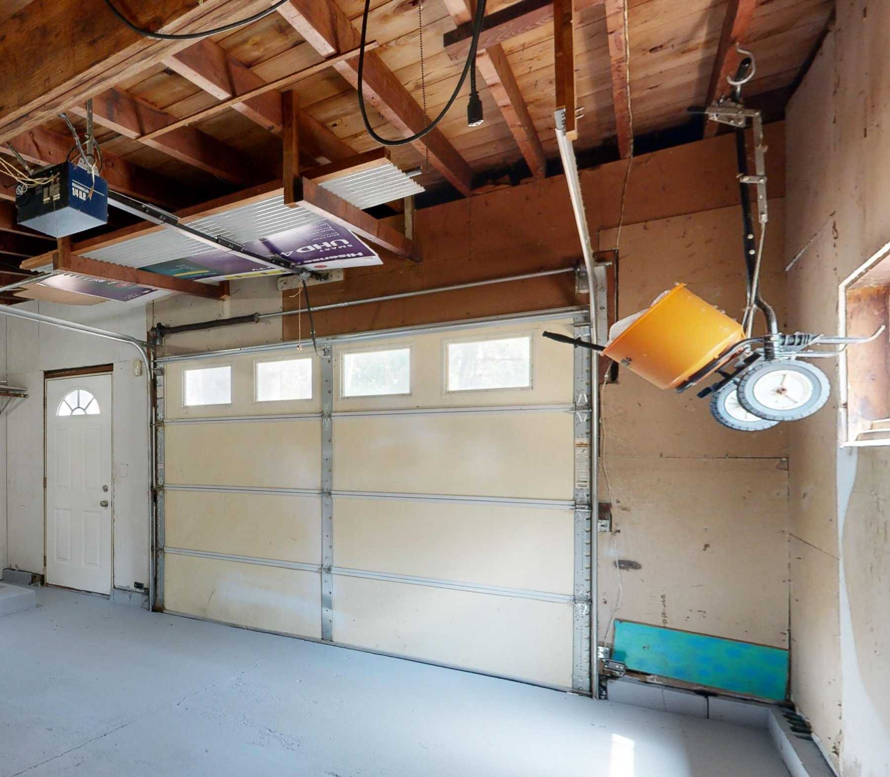 Inside a garage: a sectional garage door with a row of windows, its vertical tracks and a ceiling-mounted opener